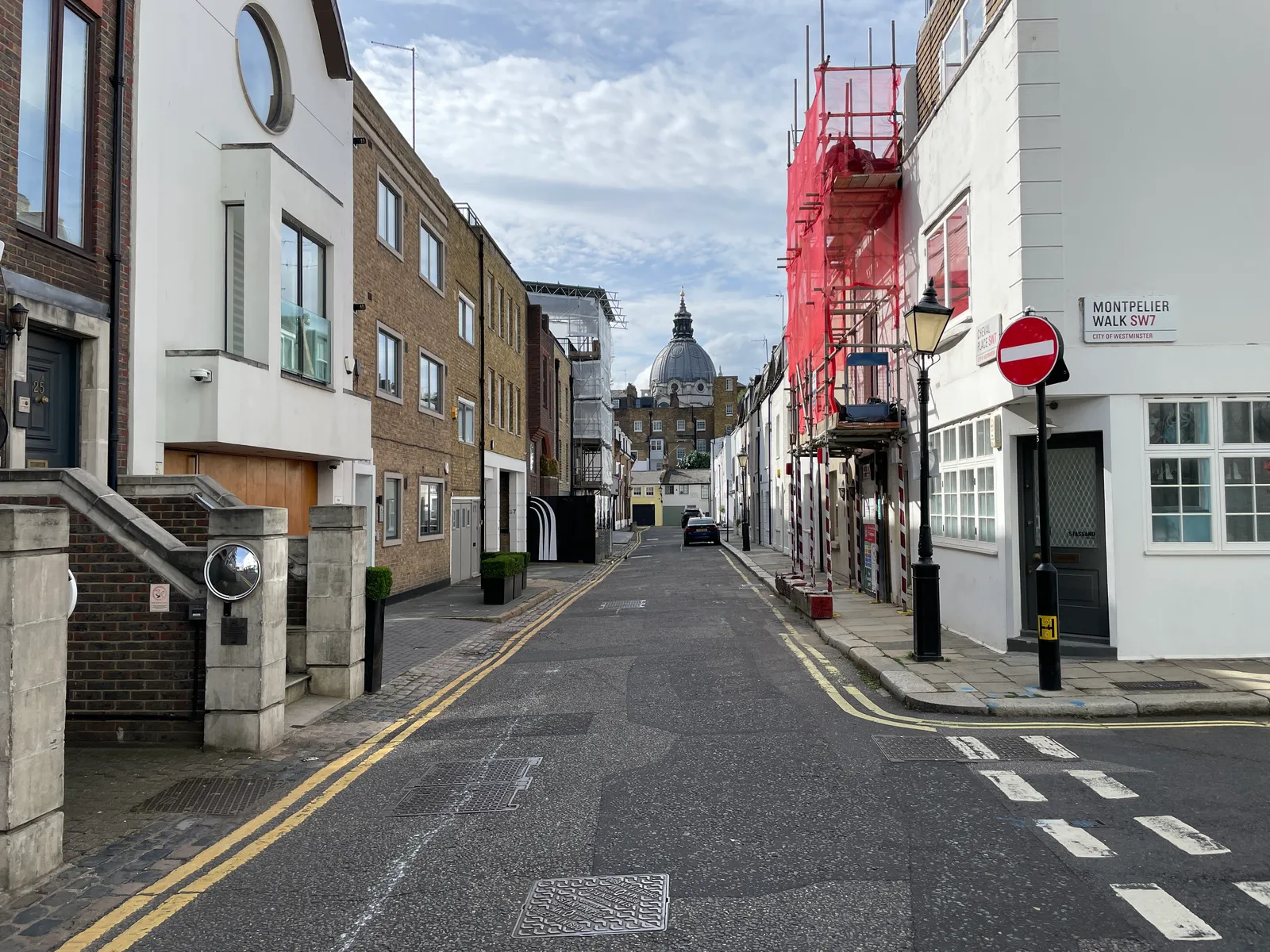 Looking down Cheval Place in Knightsbridge, a narrow street of white and brick buildings, towards a domed church