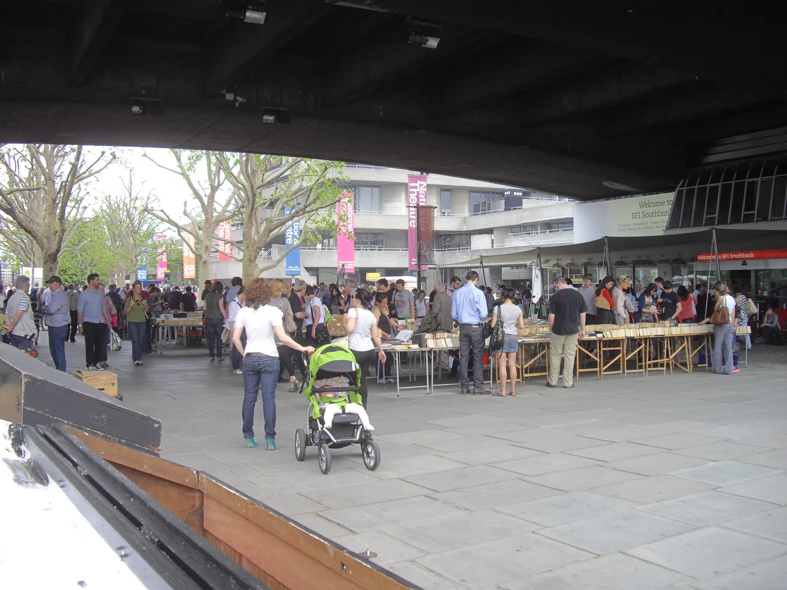 Second-hand book tables under the concrete underside of Waterloo Bridge, with browsers and the BFI Southbank entrance in the background